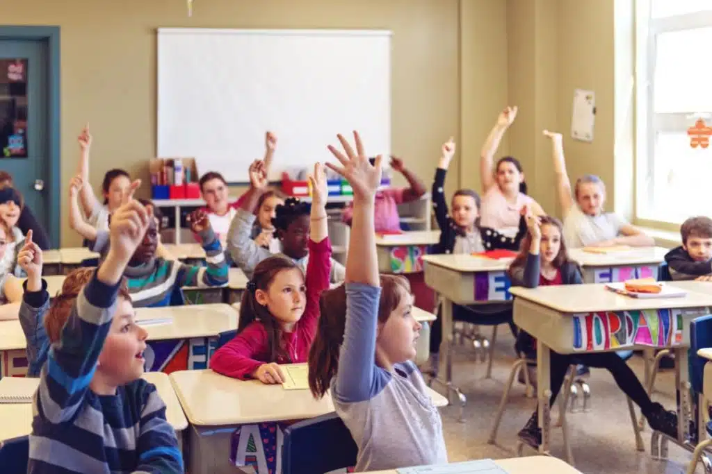 students in a classroom raise their hands
