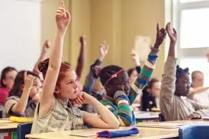 students in a classroom raise their hands