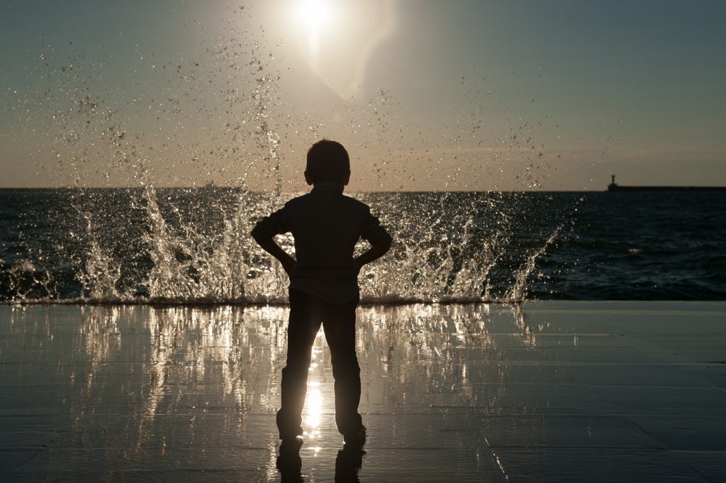 Silhouette of a small boy watching waves crash on the beach